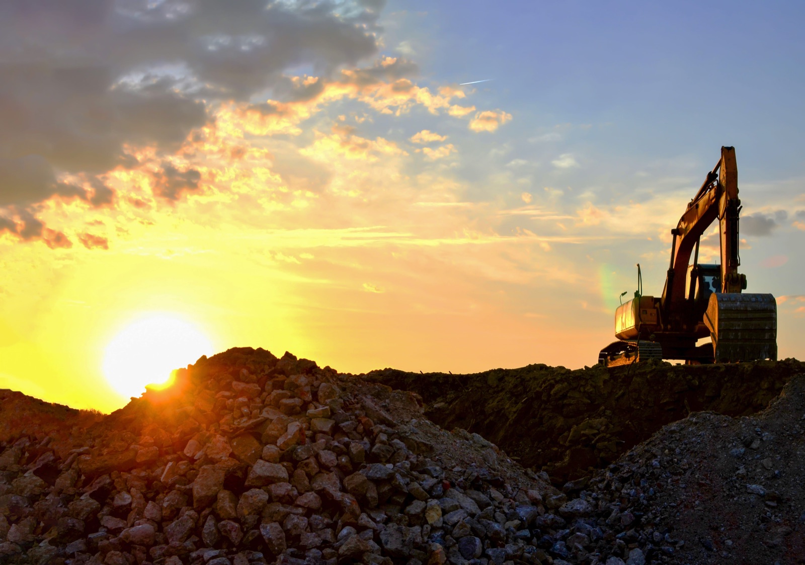 An excavator working in a quarry at sunset