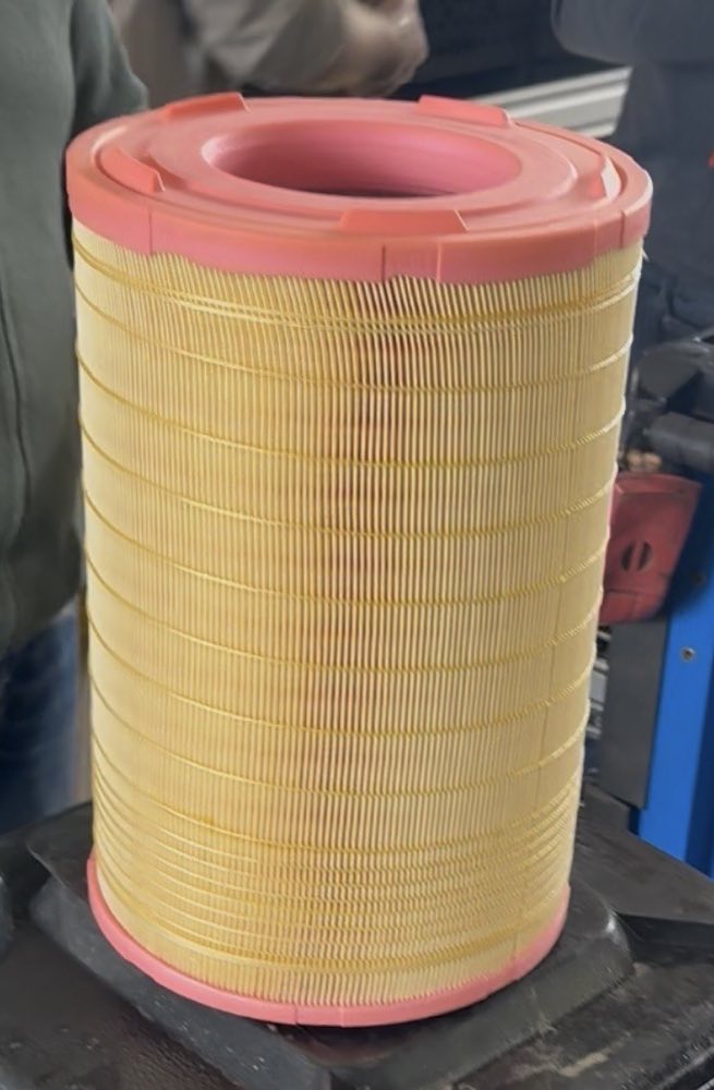 A cylindrical air filter element with pleated paper and red end caps, standing on a workbench