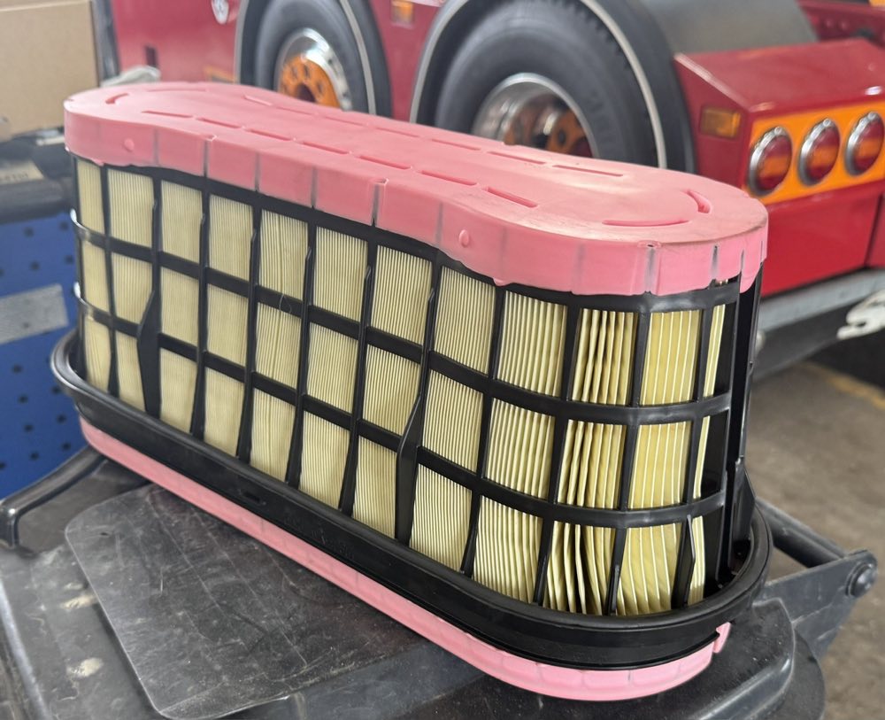 An oval air filter element in a black support cage, on a workbench in front of a red truck