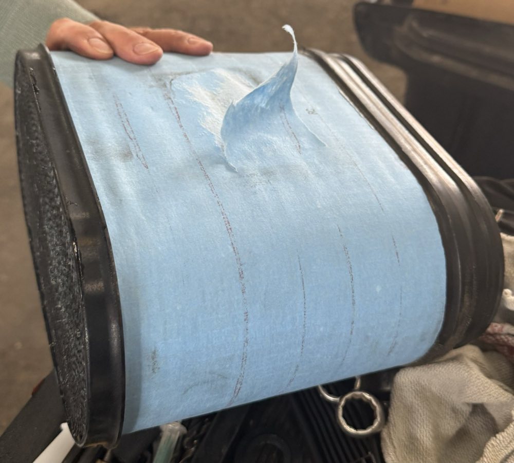 A rectangular vehicle air filter with light blue filter medium, held in a workshop