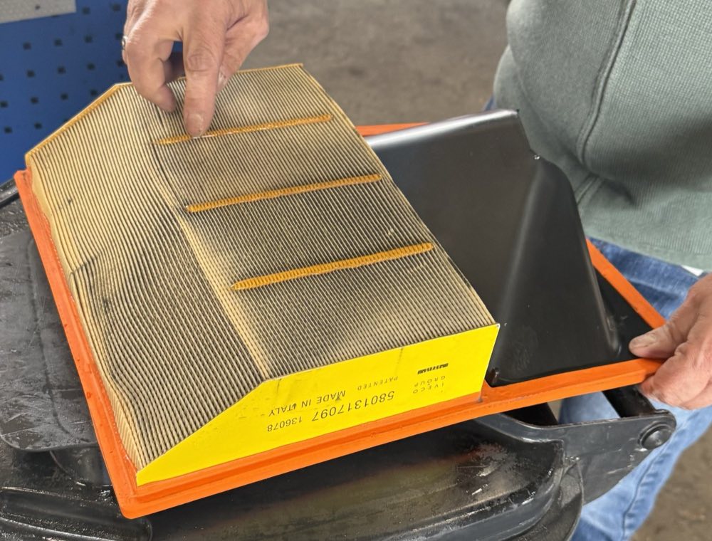 A used panel air filter with visible dust deposits across the pleats, lying in its housing